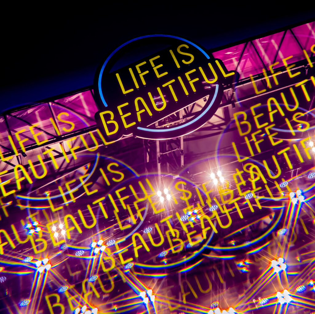 A blurred shot of a stage at Life is Beautiful festival. The image includes the festival's logo repeated with a multi-exposure effect.